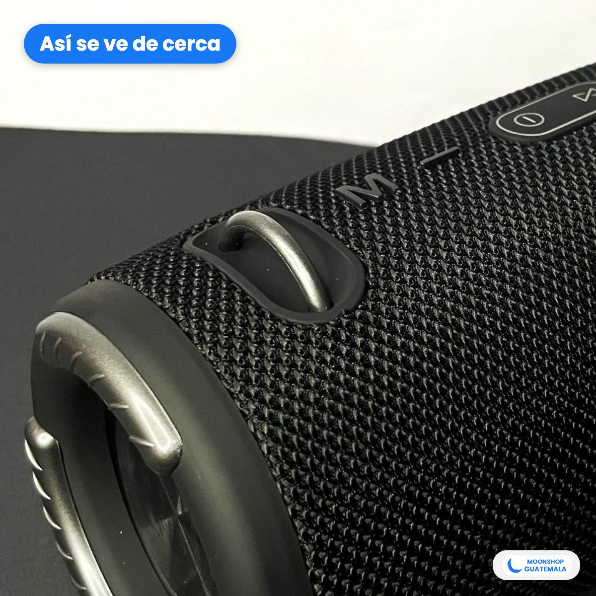 Bocina Bluetooth portátil negra vista de cerca: aro de metal, botones arriba y tela de malla