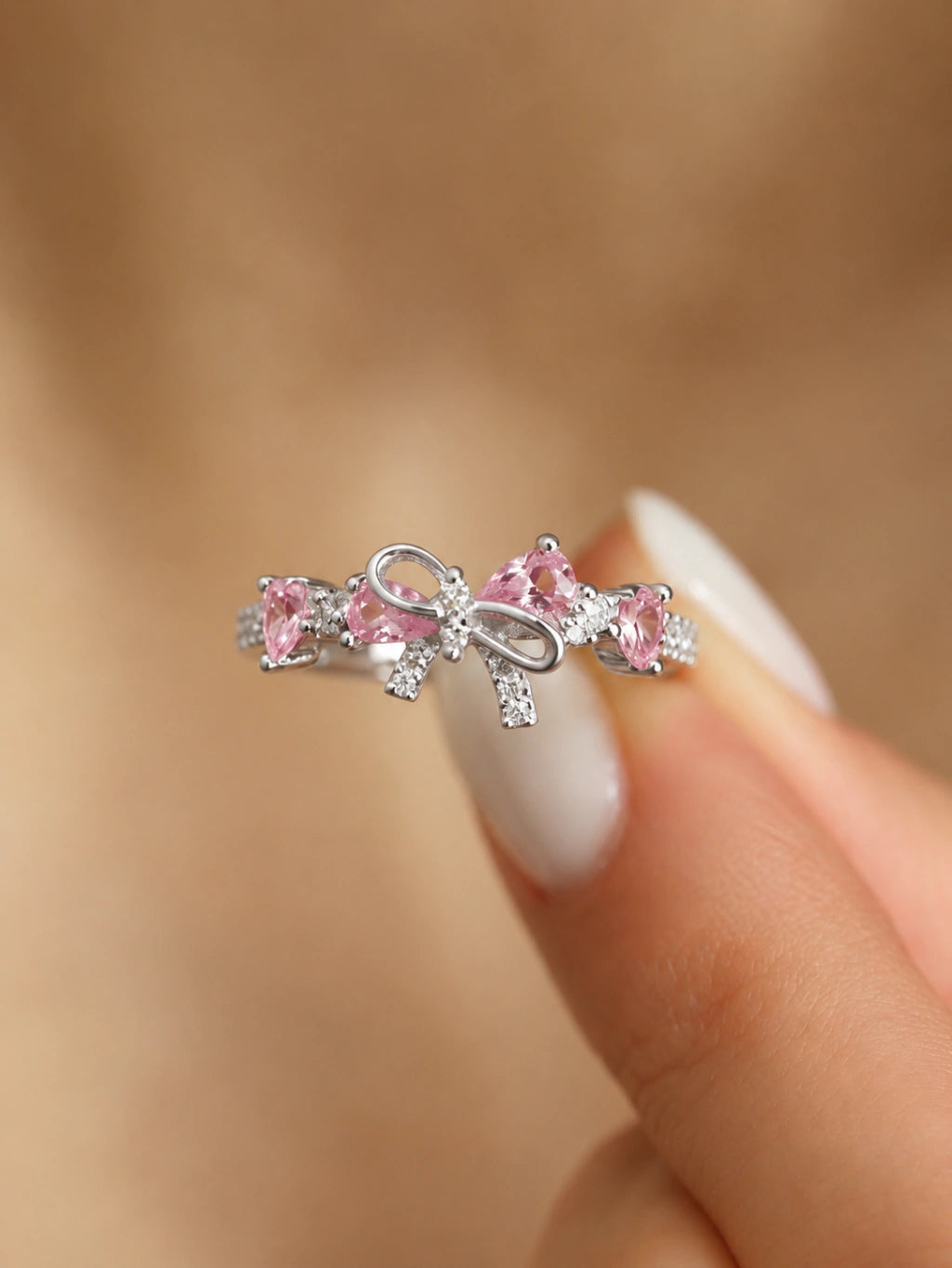 Anillo con lazo y cristales rosados sostenido entre los dedos