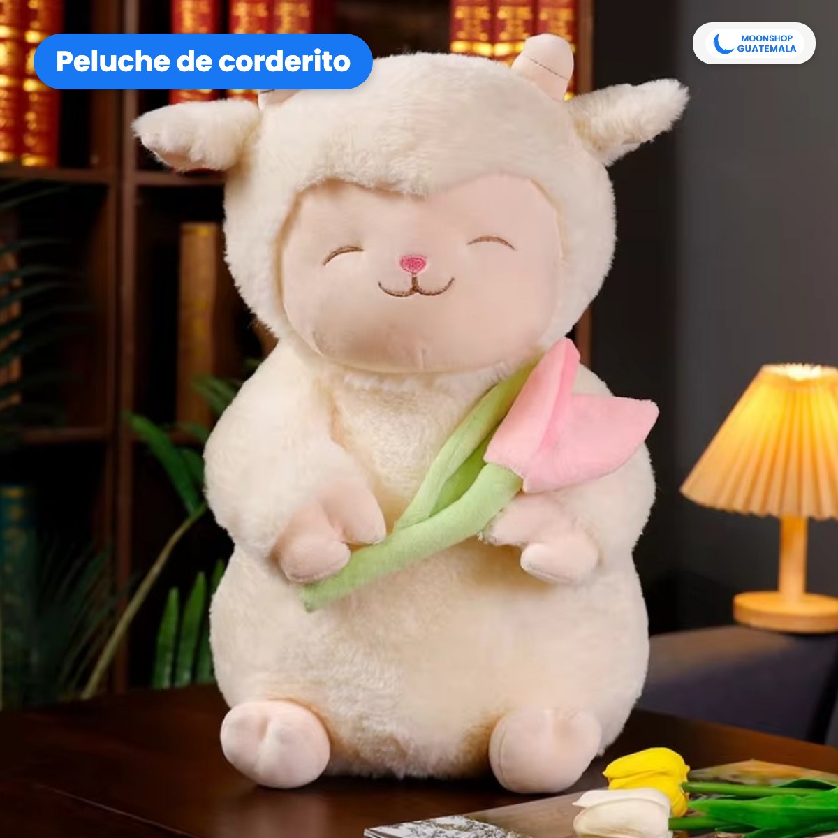 Corderito de peluche color crema con su tulipán rosado, sentado sobre un mueble junto a una lámpara