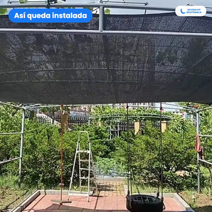 Malla sombra sarán negra instalada sobre una pérgola de tubos en un jardín, dando sombra al patio